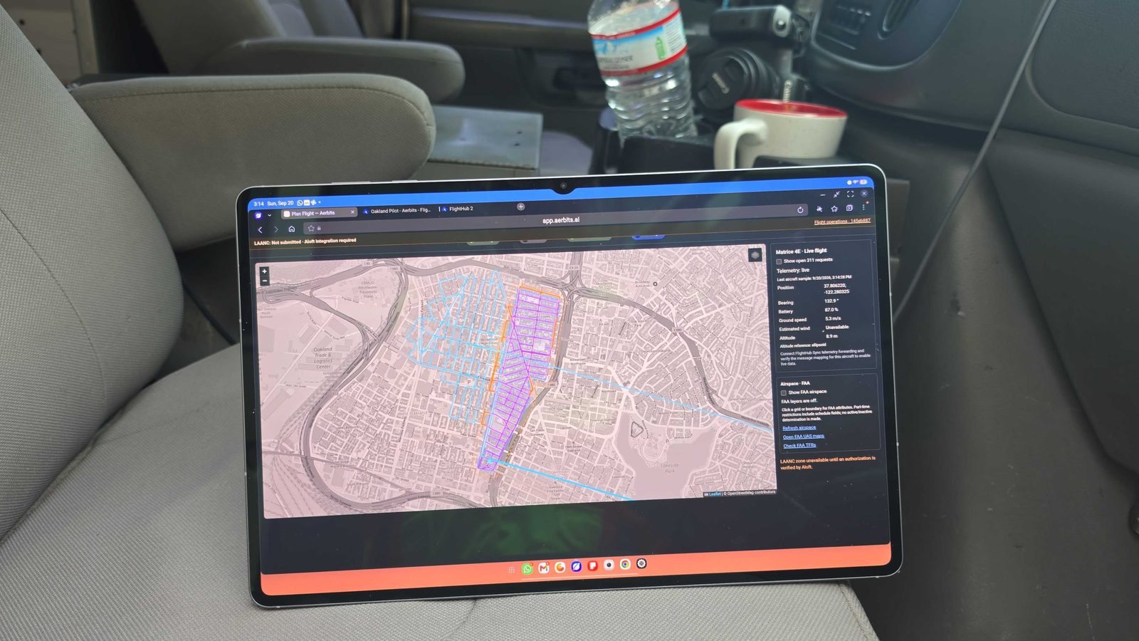 A laptop in a vehicle showing Aerbits flight planning software with survey grids over an Oakland map